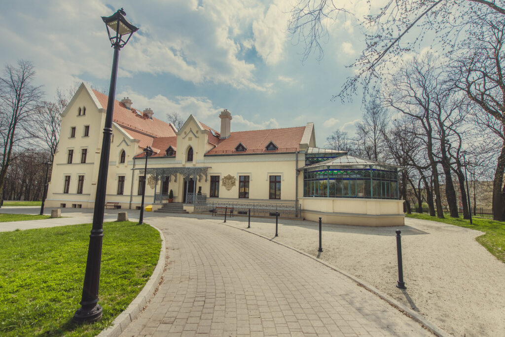 Budynek Zameczku z wiodącym do niego chodnikiem oraz z trawnikiem i drzewami