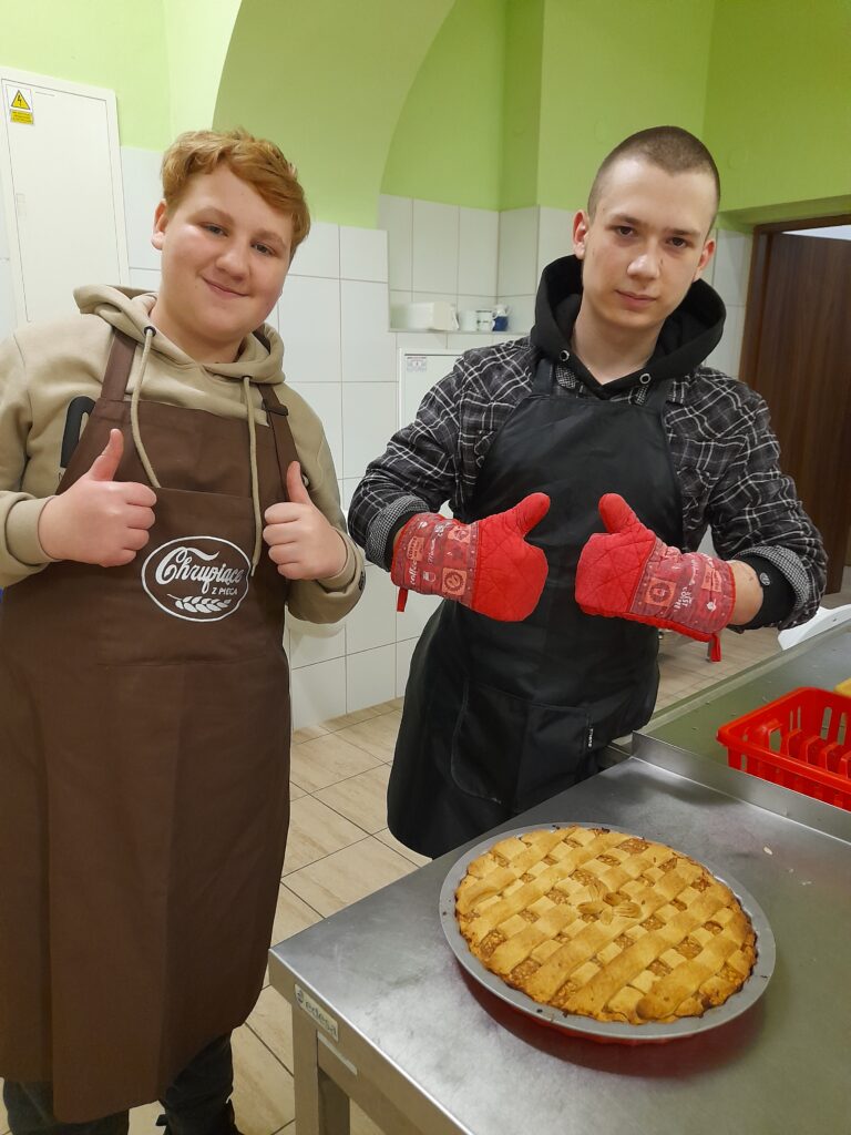 Dwóch chłopaków zadowolonych z efektu warsztatów, stojący przy jednym z wypieków