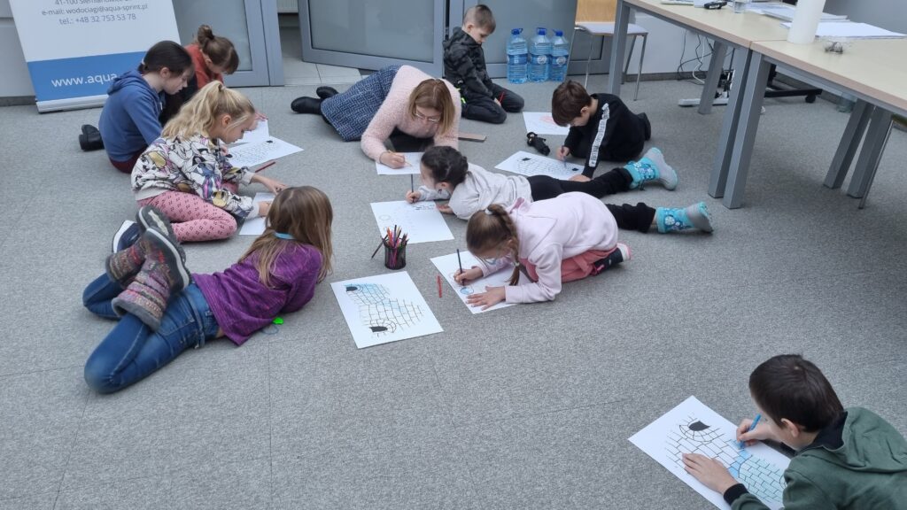 Dzieci na podłodze maja rozłożone kartki, na których tworzą swoje prace