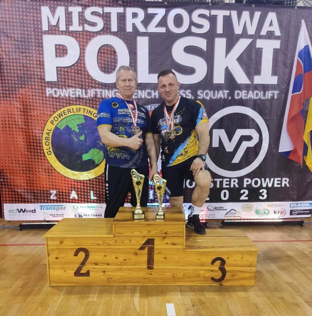 Dwaj sportowcy z medalami i pucharami stojący przy podium