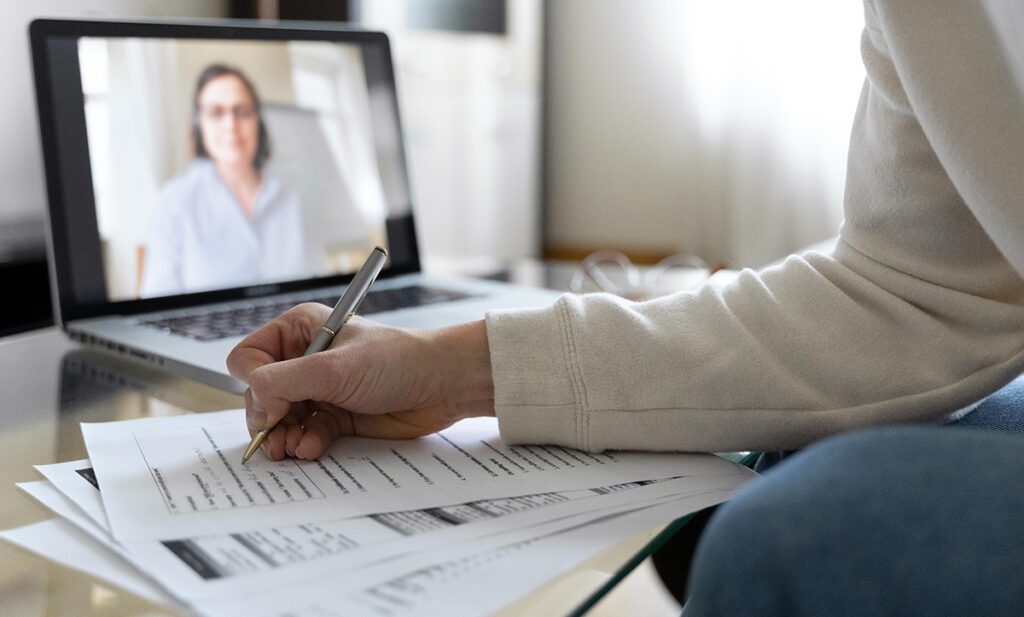 Szkolenie online przed ekranem laptopa. Na stoliku rozłożone dokumenty.