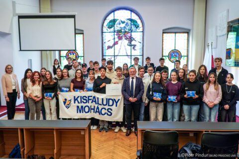 Grupa uczniów z Mohácsa i Siemianowic pozuje do wspólnego zdjęcia w sali obrad z transparentem „Kisfaludy Mohács”.