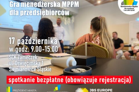 Zdjęcie przedstawia salę szkoleniową, w której grupa uczestników siedzi na krzesłach i słucha prowadzącego stojącego przy ekranie z prezentacją. Na pierwszym planie widać stół z notatnikiem, dokumentami i zestawem kart używanych w grze menedżerskiej.