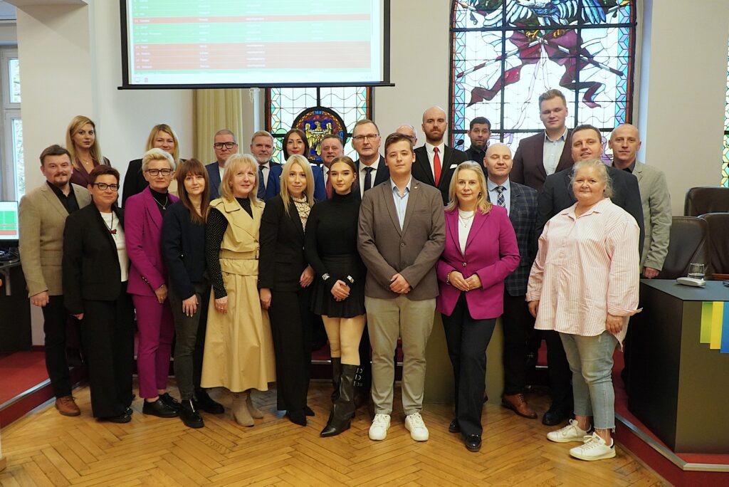 Wspólna fotografia radnych Rady Miasta oraz przewodniczącej i wiceprzewodniczącego Młodzieżowej Rady Miasta na tle witraży w Dużej Sali Ratusza.