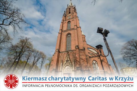 Na zdjęciu widoczny jest wysoki, neogotycki kościół z czerwonej cegły – świątynia pw. Krzyża Świętego w Siemianowicach Śląskich. Zdjęcie wykonano od dołu, ukazując imponującą wieżę i detale architektoniczne. W tle widać drzewa z wiosenną zielenią i błękitne niebo z lekkim zachmurzeniem. Na dole grafiki widnieje napis: „Kiermasz charytatywny Caritas w Krzyżu. Informacja Pełnomocnika ds. Organizacji Pozarządowych”.