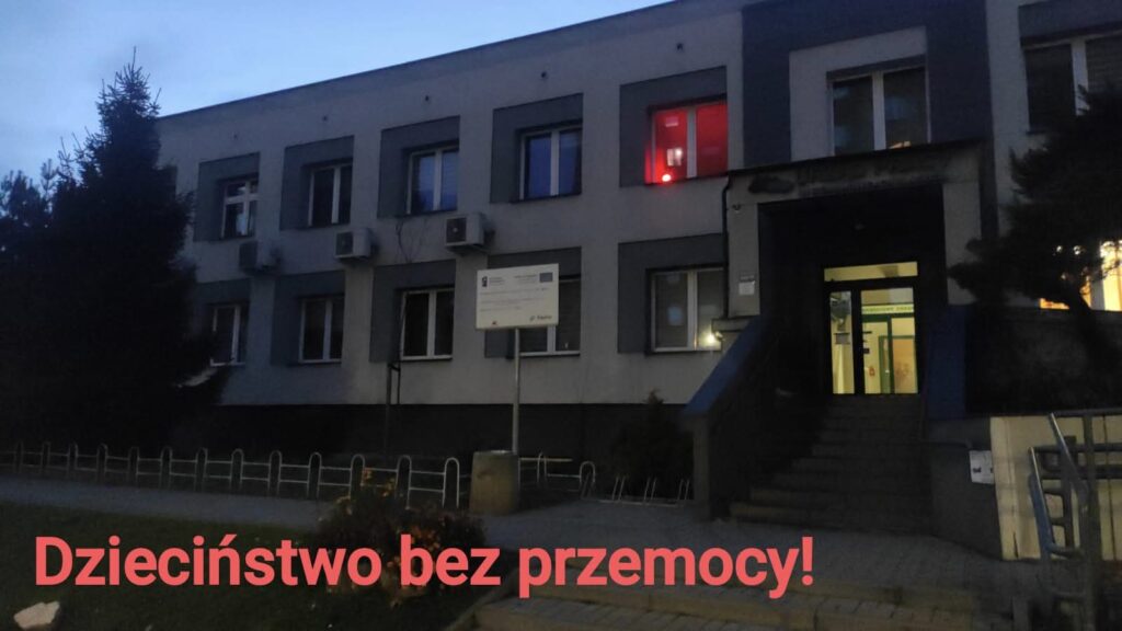 Otynkowany budynek z oknami i czerwonym światełkiem, palącym się w jednym z okien na 1. piętrze