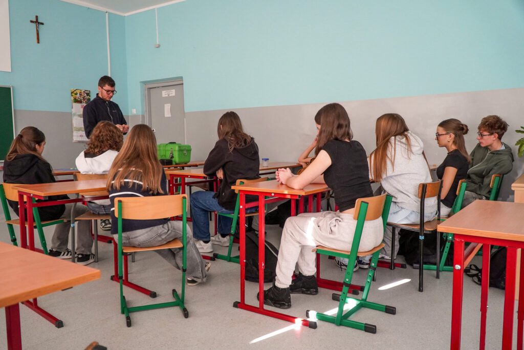 Grupa uczniów uczestniczy w spotkaniu z przedstawicielem lokalnej firmy MMJ w sali lekcyjnej.