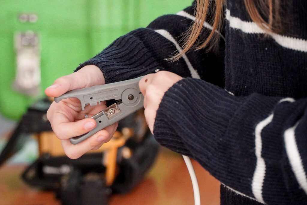 Uczennica korzysta z narzędzia do przygotowywania przewodów do zarabiania wtyczek RJ.