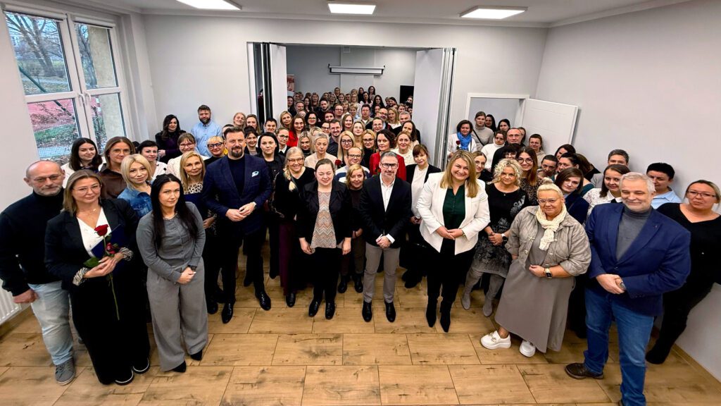 Duża grupa osób stojących w jasnej sali, pozujących do zdjęcia pamiątkowego