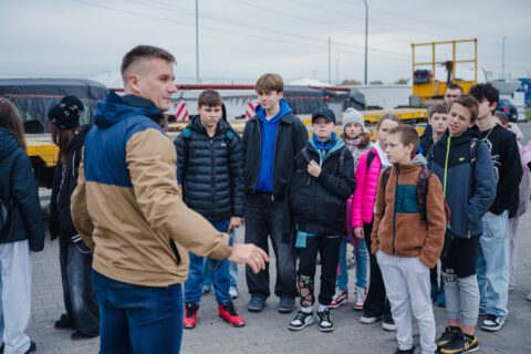 Pracownik firmy ZTE oprowadza grupę uczniów podczas zwiedzania placu transportowego.