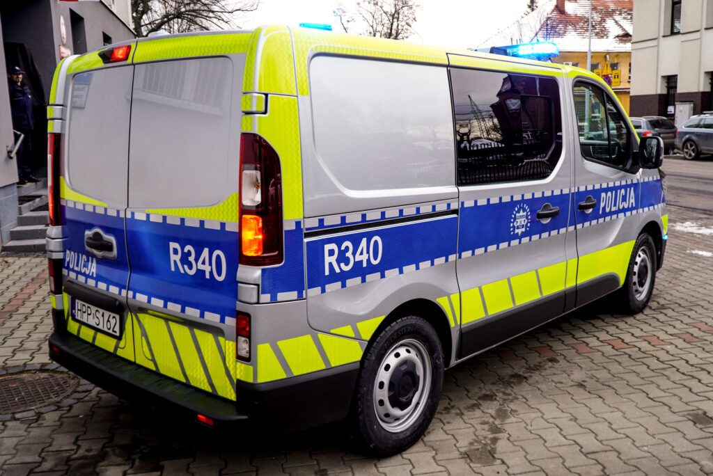 Widok radiowozu Policji od strony tylnej i bocznej. Na drzwiach oraz bokach pojazdu widoczne są oznaczenia „Policja” i numer jednostki. Samochód wyposażony jest w światła ostrzegawcze oraz elementy odblaskowe zwiększające bezpieczeństwo na drodze.