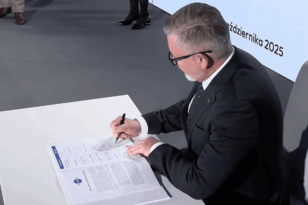 Adam Skowronek, Sekretarz Miasta Siemianowice Śląskie, podpisuje Deklarację Prostego Języka przy białym stole. W tle widoczna scena wydarzenia oraz ekran z nazwą inicjatywy promującej prostą komunikację.