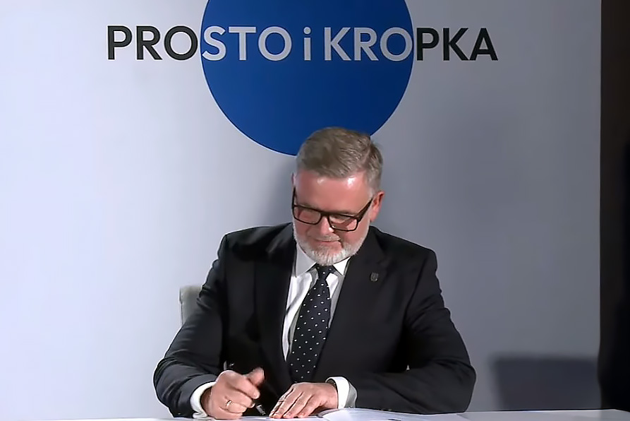 Sekretarz Miasta Siemianowice Śląskie Adam Skowronek siedzi przy stole i składa podpis na Deklaracji Prostego Języka. Ubrany w ciemny garnitur, pochylony nad dokumentem. Zdjęcie wykonane podczas oficjalnej ceremonii podpisania Deklaracji.