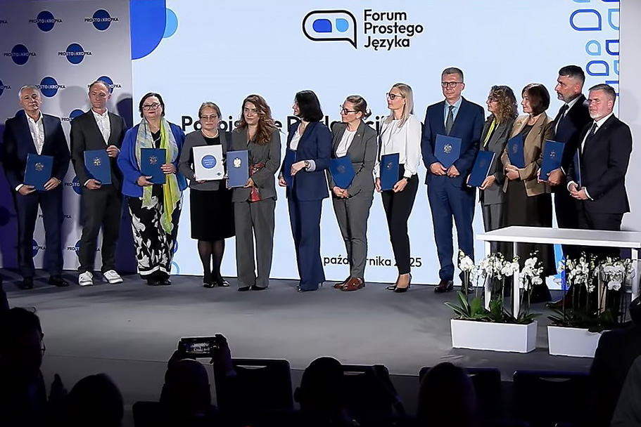 Grupowe zdjęcie sygnatariuszy Deklaracji Prostego Języka stojących na scenie i trzymających teczki z dokumentami. Wśród nich przedstawiciele ministerstw, urzędów centralnych, samorządów i instytucji publicznych. Zdjęcie wykonane po zakończeniu ceremonii podpisania Deklaracji.