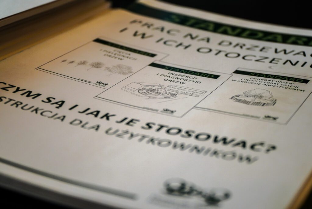 Zbliżenie na wydrukowane materiały informacyjne zespołu „Siemianowickie Geranium”, dotyczące standardów ochrony drzew i zieleni w procesach inwestycyjnych. Na dokumentach widoczne są schematy i tytuły opracowań poświęconych diagnostyce oraz ochronie drzew.