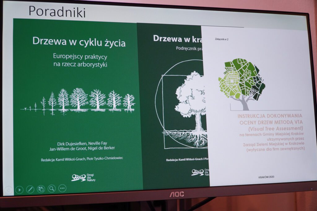 Zbliżenie na ekran prezentacyjny z widocznymi tytułami publikacji poświęconych ocenie drzew, arborystyce i standardom pielęgnacji zieleni. Slajd stanowi element omawianej prezentacji eksperckiej.
