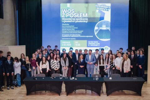 Grupa młodzieży oraz zaproszeni goście stoją razem na scenie do wspólnego zdjęcia. Wszyscy ustawieni są w kilku rzędach, a w tle widoczny jest ekran z nazwą wydarzenia i logotypami organizatorów.