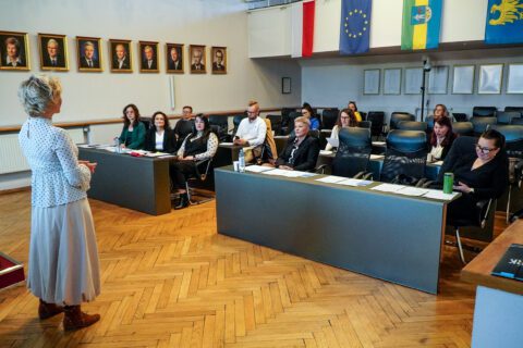 Katarzyna Zapart prowadzi prezentację dla przedsiębiorców siedzących przy stołach w sali sesyjnej Urzędu Miasta.