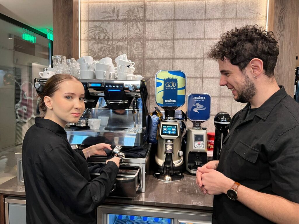 Uczennica ZS Cogito szkoli się przy ekspresie do kawy pod okiem doświadczonego baristy.