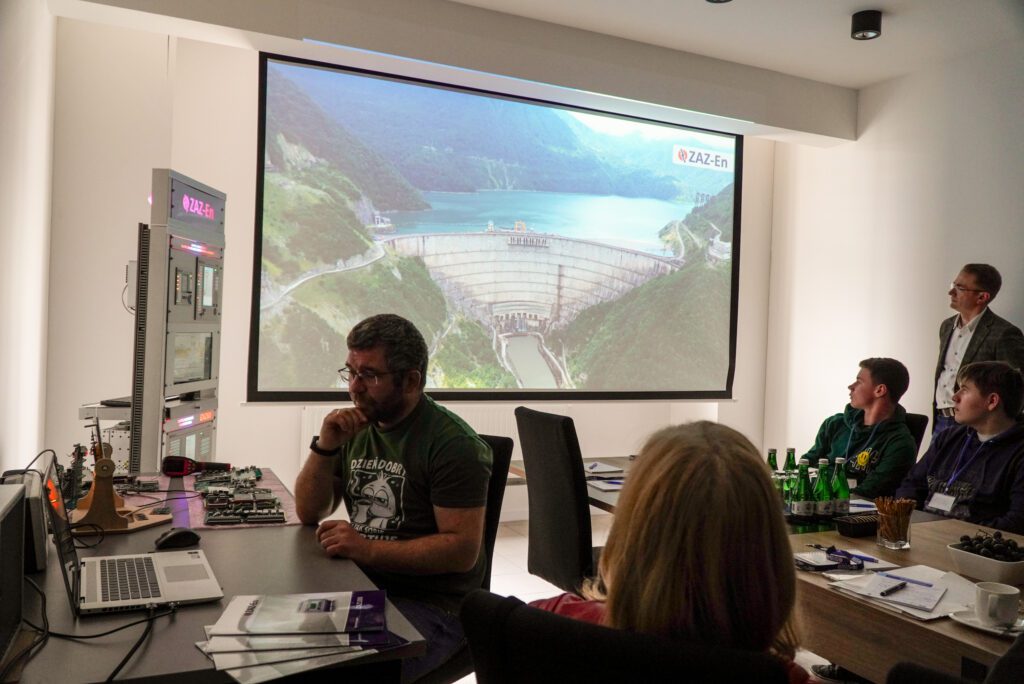 Na ekranie wyświetlona zapora wodna, uczestnicy oglądają prezentację.