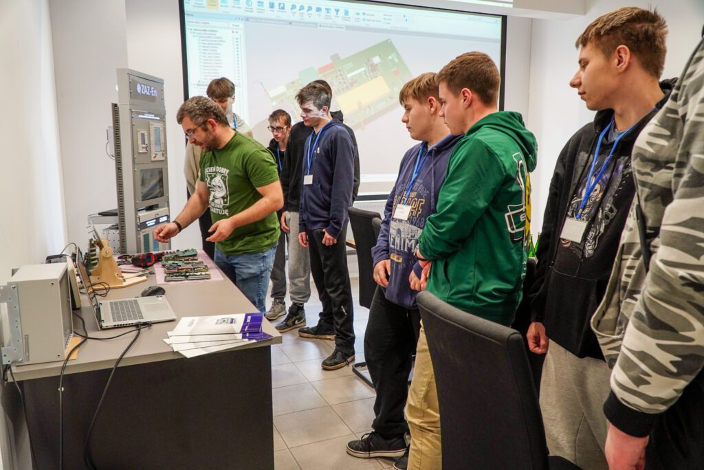 Uczniowie stoją przy stole i oglądają sprzęt prezentowany przez pracownika firmy.