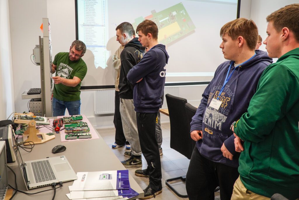 Uczniowie stoją przy stole i oglądają sprzęt prezentowany przez pracownika firmy.