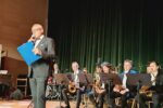 Grzegorz Franki, prezes Związku Górnośląskiego, stoi na scenie Parku Tradycji i przemawia do mikrofonu, trzymając niebieską podkładkę z dokumentami. Jest ubrany w ciemny garnitur z fioletową muchą i poszetką. W tle, za jego plecami, siedzą muzycy orkiestry Happy Big Band z instrumentami dętymi, gotowi do występu.