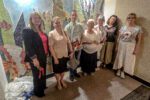 Grupa uczestników uroczystości pozuje do wspólnego zdjęcia na tle kolorowej mozaiki przedstawiającej podwodny świat. Wśród nich znajduje się autor pracy, przedstawicielki placówki oraz zaproszeni goście.