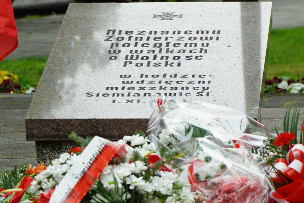 Zbliżenie na pomnik poświęcony Nieznanemu Żołnierzowi poległemu w walkach o wolność Polski. U stóp pomnika znajdują się biało-czerwone wieńce i wiązanki kwiatów złożone podczas uroczystości.
