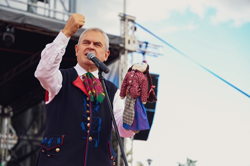 Marek Szołtysek prowadzi animacje dla publiczności na scenie, trzymając tradycyjną lalkę i opowiadając o dawnych śląskich zabawach.