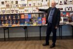 Kolekcjoner Henryk Cymbała, wskazuje dłonią wystawę