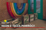 Wnętrze zniszczonego budynku z kaflami na ścianie. Na zabrudzonej posadzce leży kolorowy neon w kształcie łuku tęczy oraz kasetony z zielonymi literami napisu. Obok znajdują się przeszklone, zielone drzwi.