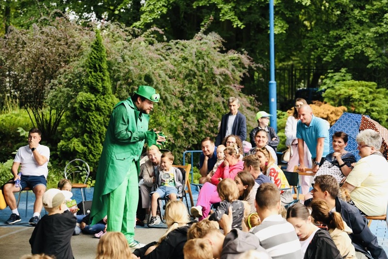 Aktor w zielonym kostiumie rozmawia z dziećmi siedzącymi przed sceną podczas spektaklu „Księżniczka i EKOżaby”.