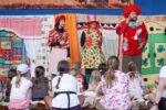 Troje aktorów w kolorowych kostiumach występujących przed dziećmi podczas finałowego Teatralnego Lata pod Chmurką.