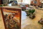 Stół do gry Warhammer Fantasy Battle z rozstawionymi figurkami armii, budynkami i elementami terenu podczas turnieju ŚlunskHammer w Parku Tradycji.