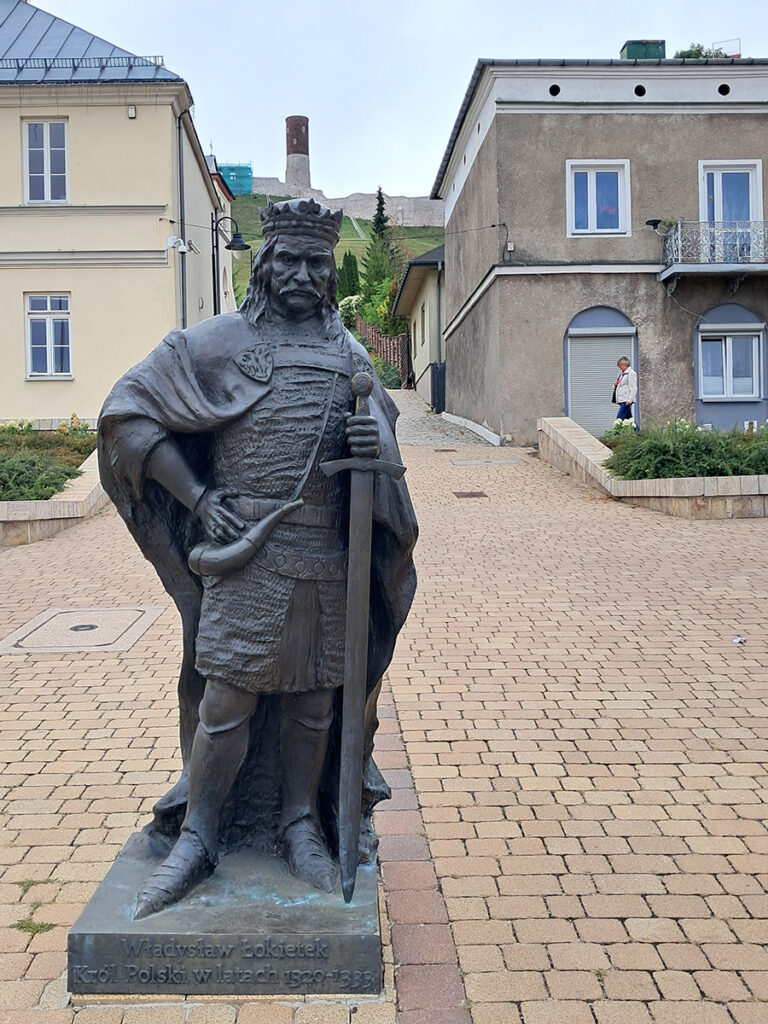 Pomnik króla Władysława Łokietka w Chęcinach, z ruinami Zamku Królewskiego widocznymi w tle.