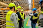 Grupa uczniów w kaskach i kamizelkach odblaskowych podczas zwiedzania hali produkcyjnej Aperam